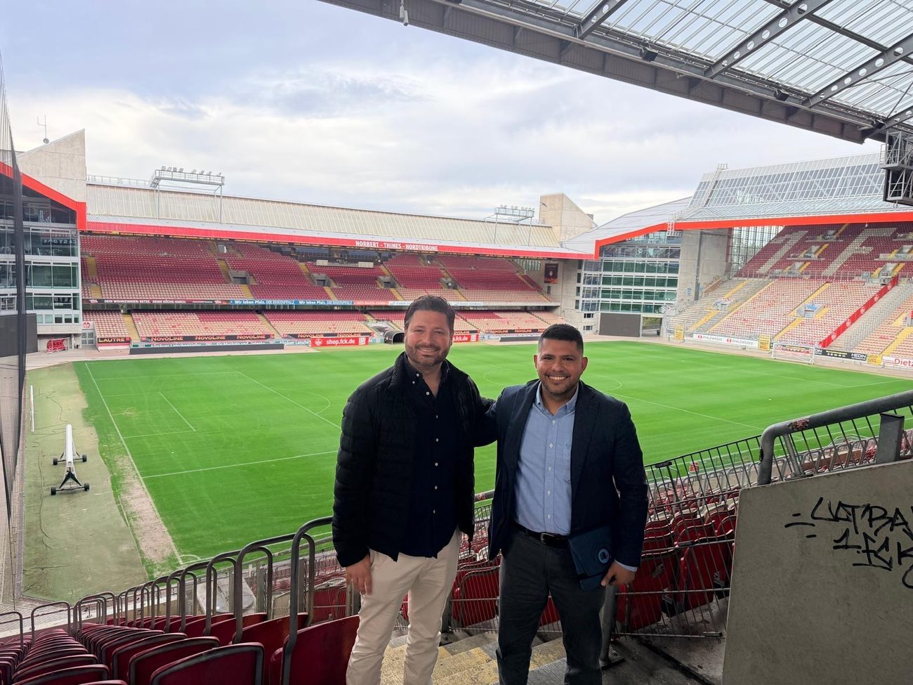 Two men standing in the stand of the Fritz-Walter-Stadion in Kaiserslautern with the pitch behind them