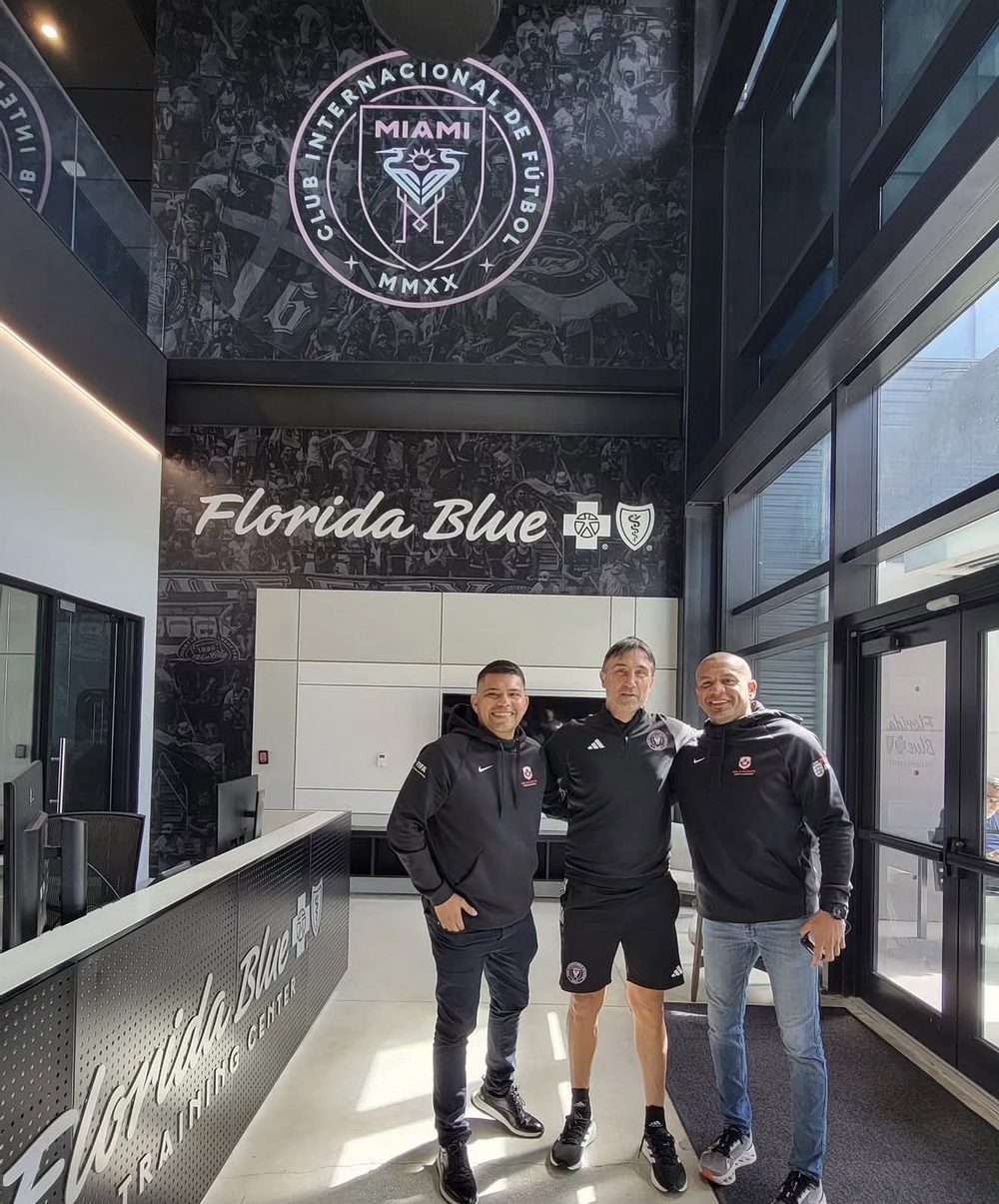 Three men standing in the lobby of the Inter Miami CF training centre under the club crest